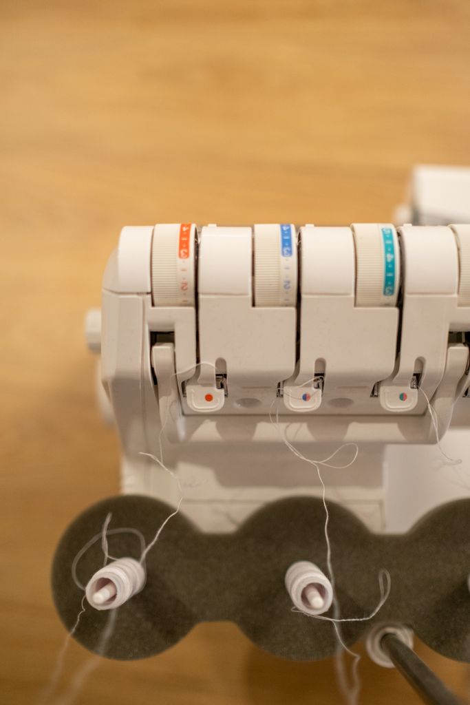 Close-up view of an overlocker sewing machine with colorful thread spools and tension dials.